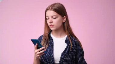 Pembe arka planda telefonla konuşan tatminsiz bir kızın 4K videosu. Tatminsizlik duygusu kavramı.