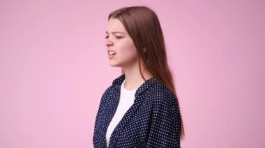 Sinirli ve pembe arka planda tırnaklarını yiyen bir kızın 4K videosu. Üzüntü kavramı