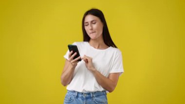 Sarı arka planda izole edilmiş telefonu kullanan hoş bir kadının 4K videosu. Teknoloji kavramı.