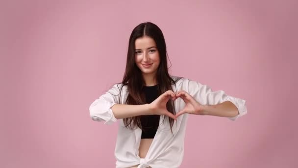 4K个微笑的女性视频 在粉色背景下表现出心脏的形状 爱情的概念 — 图库视频影像