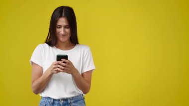 4K video 'da güzel bir kadın telefon kullanıyor ve sarı arka planda bir şey sunuyor. Sunum kavramı.