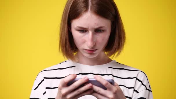 黄色の背景に隔離された彼女の携帯電話で何かを見てかわいい女性の4Kビデオ 技術の概念 — ストック動画