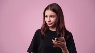 Pembe arka planda izole edilmiş telefonu kullanan hoş bir kadının 4K videosu. Teknoloji kavramı.