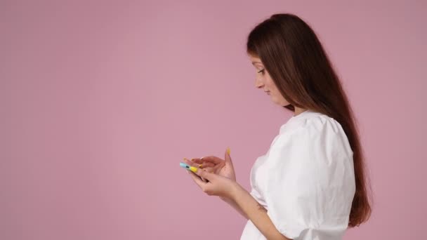 ピンク色の背景に隔離された電話での可愛い女のテキストメッセージの4K動画 技術の概念 — ストック動画
