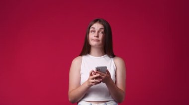 Kırmızı arka planda izole edilmiş telefonu kullanan hoş bir kadının 4K videosu. Teknoloji kavramı.