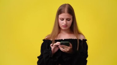 Sarı arka planda izole edilmiş telefonundan bir şey izleyen hoş bir kadının 4K videosu. Teknoloji kavramı.