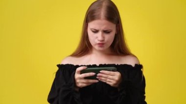 Sarı arka planda izole edilmiş telefonundan bir şey izleyen hoş bir kadının 4K videosu. Teknoloji kavramı.