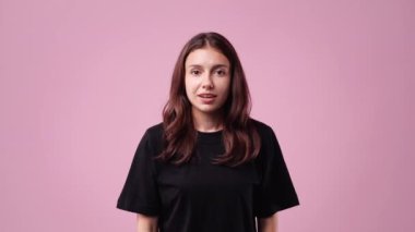 Siyah tişörtlü düşünceli bir kadının pembe arka planda gülümsediği 4K video. Neşe kavramı.