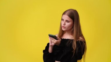 Sarı arka planda izole edilmiş telefonundan bir şey izleyen hoş bir kadının 4K videosu. Teknoloji kavramı.
