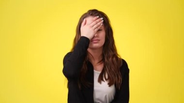 Sarı arka planda elleri ile yüzünü kapatan huysuz kadının 4K videosu. Huysuz kadın kavramı.