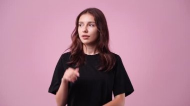 Siyah tişörtlü düşünceli bir kadının pembe arka planda gülümsediği 4K video. Neşe kavramı.