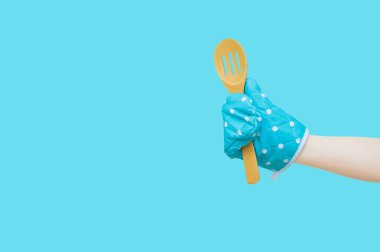 Wooden spoon and oven mitt in the hand of a Caucasian woman. Turquoise background isolate.