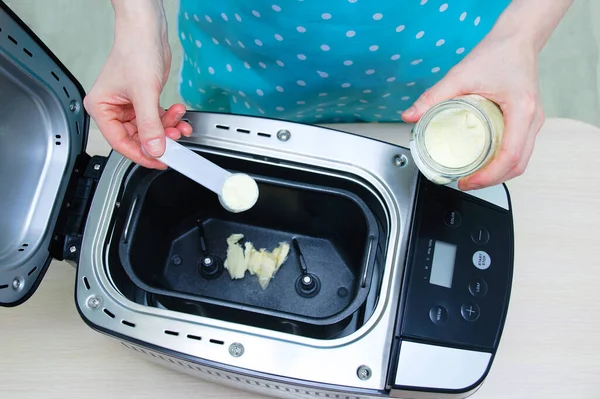 Caucasian woman pours powdered milk into a bread machine. View from above.