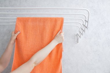 Metal duvara monte edilmiş çamaşır kurutma makinesine havlu asıyor. Beyaz bir kadının elleri.