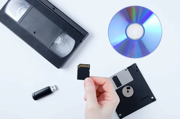 손에는 메모리 카드를 비디오 카세트 플래시 드라이브 배경의 플로피 디스크 — 스톡 사진