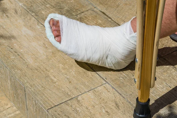 Man with broken leg in white plaster cast go down steps with crutches. Fracture of leg after falling off the steps. The leg turned up and broke