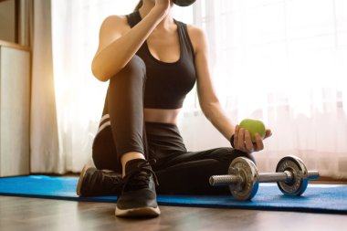 Spor salonunda egzersiz yapan bir kadın, sağlıklı olması için spor yapan genç bir kadın. Elinde yeşil elma tutuyor..