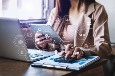 Modern ofiste cep telefonu kullanan bir kadının elleri dizüstü bilgisayarı ve dijital tablet bilgisayarı ile sabah saatlerinde ofiste VR simgesi diyagramı kullanıyor.