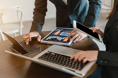 Ofis masasında akıllı telefon ve dizüstü bilgisayarı olan iş belgeleri ve sabah ışığında arka planda veri tartışması yapan iki iş arkadaşı.