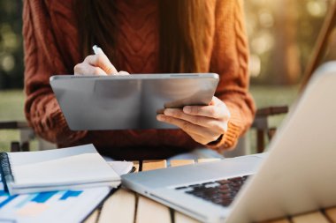 Akıllı telefon ve dijital tabletli ofis masasında iş belgeleri ve çalışan kadın ve finans grafiği