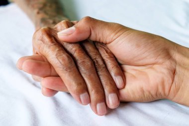 Yaşlı bir adam ve bir adamın elleri hastanedeki beyaz yatakta.
