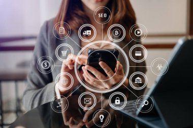 İş kadını ya da tasarımcı cep telefonu, dizüstü bilgisayarı ve dijital tablet bilgisayarı kullanıyor ve sabah kalktığında sanal simgeler ağı diyagramı ile birlikte masadaki belgeyi kullanıyor.