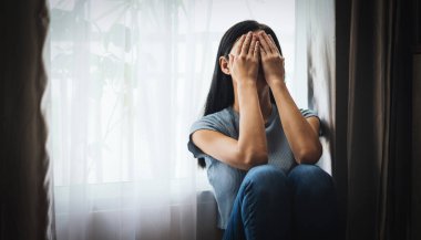 Depresyondaki ağlayan kadın evde otururken elleriyle yüzünü kapatıyor. 