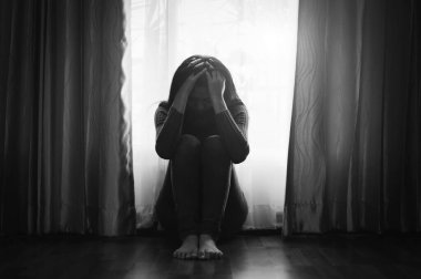 Depresyondaki ağlayan kadın evde otururken elleriyle yüzünü kapatıyor. 