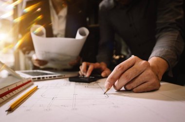 Ofis masasında çalışan mimarlar. Masada kağıt inşa planıyla birlikte çalışıyorlar. 