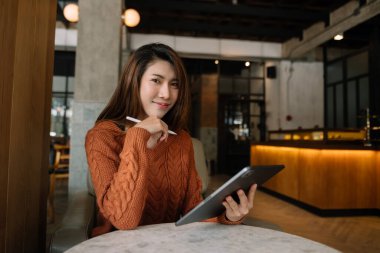 Kafede dijital tablet kullanan gülümseyen Asyalı kadın 