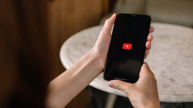 Woman holding iPhone with video service YouTube on the screen