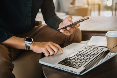 Businessman typing on laptop keyboard computer and holding smartphone 