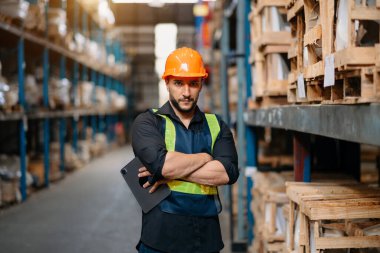 Male factory manager using tablet in warehouse shelf looking at camera.Products and corrugated cardboard.looking at camer