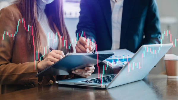 Two professional business partners working on technical price graph and indicator, red and green candlestick chart and stock trading computer