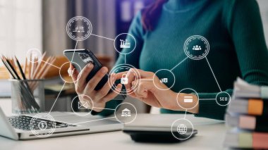 İş kadını, bilgisayarla masaya oturup cep telefonu kullanırken satış verilerini ve ekonomik büyümeyi analiz ediyor.