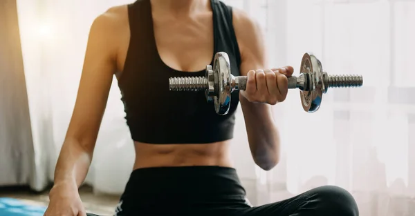 Determined woman losing weight at home and exercising with dumbbells. Sport and recreation concept. Beautiful woman in sportswear