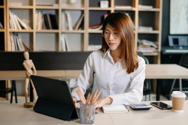 Ofisteki ahşap masada otururken tablete yazı yazan güzel Asyalı kadın.