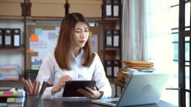 Ofis masasında dizüstü bilgisayarda çalışan Asyalı kadın dijital tabletle notlar alıyor. 