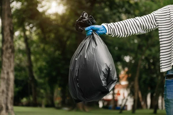 woman in gloves holding black garbage bag, pollution and ecology concept