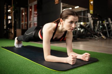 Genç bir kadın spor salonunda yerde şınav çekiyor.