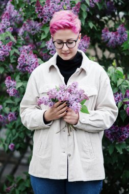Mor arka planda pembe leylak çiçekleri ve çiçek açan leylak dalıyla çekici genç bir kadın.