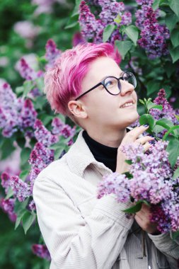 Mor arka planda pembe leylak çiçekleri ve çiçek açan leylak dalıyla çekici genç bir kadın.