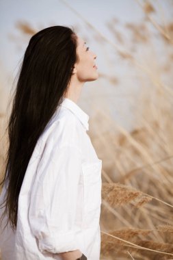 Güz tarlasında saman yığınıyla poz veren pamuklu bir elbise giyen güzel bir manken. Boho tarzı kıyafetler..