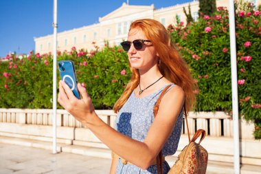 Genç bir kadın akıllı telefonuyla selfie çekiyor ve gülümsüyor.