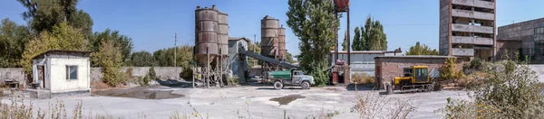 Panoramic photo of an old cement factory. An old dump truck and tractor made in the USSR.