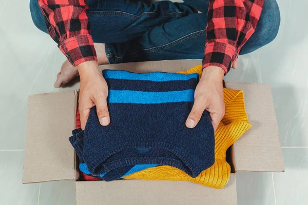 man holding a crate of second-hand clothes unused clothes