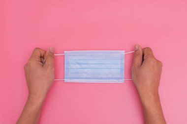 Pembe arka planda mavi bir maske tutuyor.