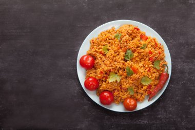 Mavi bir tabakta pirinç, domates ve acı biber, çatal, siyah bir arka planda keten peçetede kaşık. Afrika 'nın ulusal mutfağı.