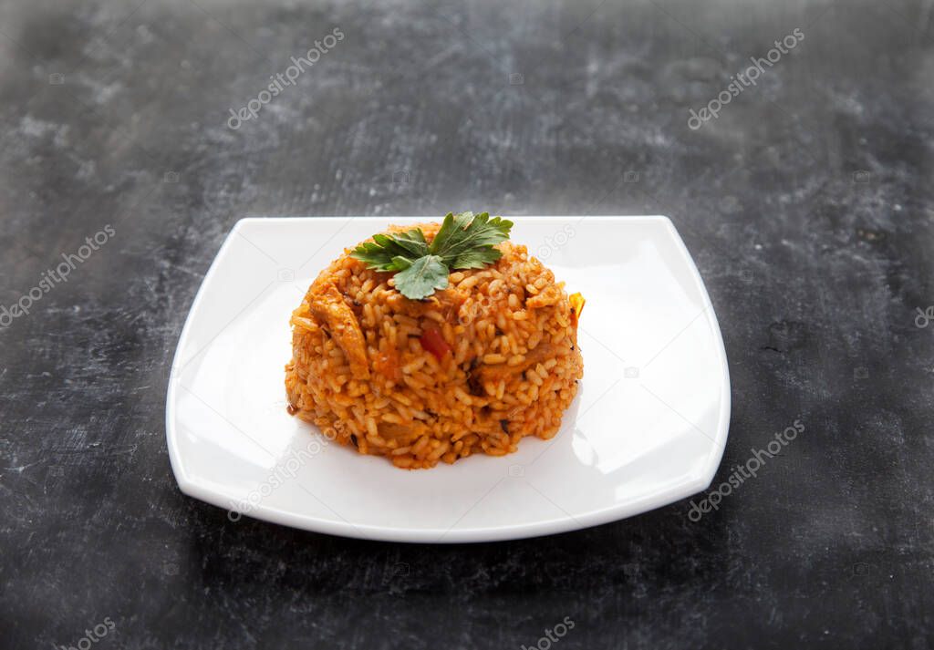 Jollof rice with parsley on a plate on a black background. National cuisine of Africa.