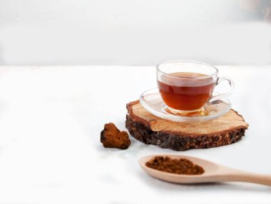 Cam bardaktaki Chaga içkisi arka planda kesilmiş tahta bir testerenin üzerinde duruyor. Sağlık konsepti. Vejetaryenlik. Kürekleri kopyala.